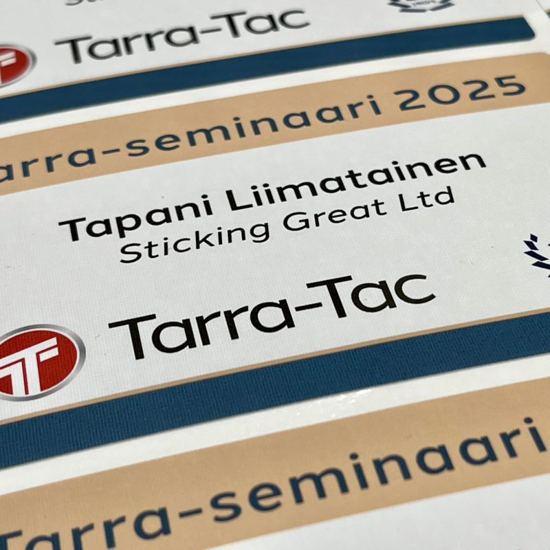 Tekstiilitarra yrityksen logolla, nimitarra kankaasta ja vaihtuvalla datalla, irrotettavalla liimalla ilman liimajäämiä